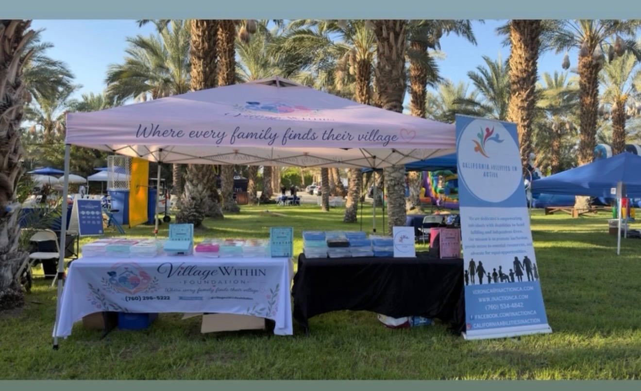 Village Within Foundation booth at a community event, with a banner reading Where every family finds their village.